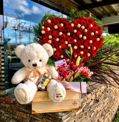 Corazón de rosas y chocolates con detalle de oso peluche.